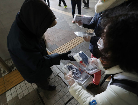 せっけんやマスクなどの支援物資が入った袋を配るボランティア（右）＝２０２０年１２月５日、東京都新宿区