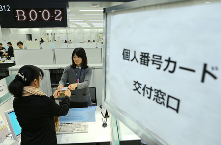 自治体窓口で個人番号カード（マイナンバーカード）を受け取る女性（左）＝２０１６年１月、東京都内