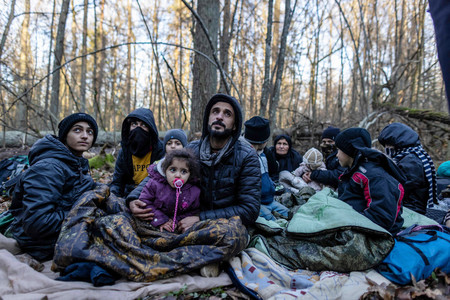 ９日、ポーランドの対ベラルーシ国境付近の森林で座り込むイラクから来たクルド人家族（ＡＦＰ時事）
