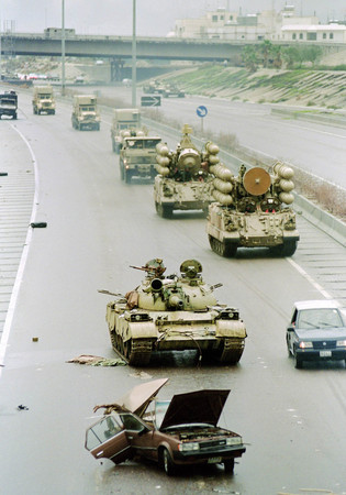 クウェート撤退に際し遺棄されたイラク軍のソ連製戦車の横を通る多国籍軍の車列＝１９９１年２月、クウェート市（ＡＦＰ時事）