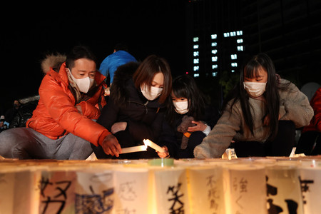 阪神大震災から２７年を迎え、追悼の集いで紙灯籠に火をともす家族＝１７日午前、神戸市中央区の東遊園地