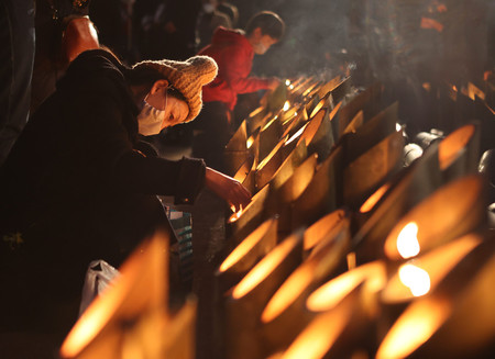 阪神大震災から２７年を迎え、追悼の集いで竹灯籠に火をともす女性＝１７日午前、神戸市中央区の東遊園地