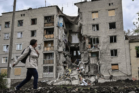 ２２日、攻撃で破壊されたウクライナ東部ドネツク州バフムトの住宅前を歩く女性（ＡＦＰ時事）