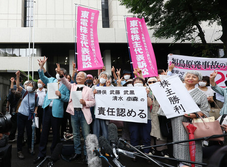 判決後、裁判所の前で「株主勝利」などと書かれた紙を掲げる原告ら＝１３日午後、東京都千代田区