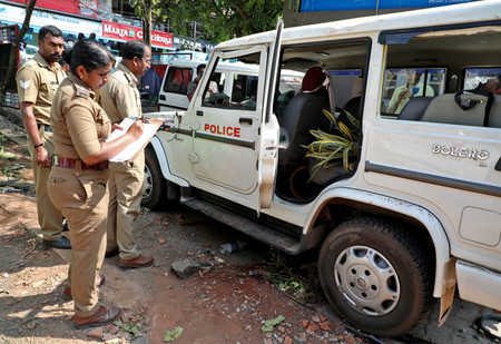 ２８日、インド南部ケララ州で、地元住民との衝突により破壊された車を調べる警官（ロイター時事）