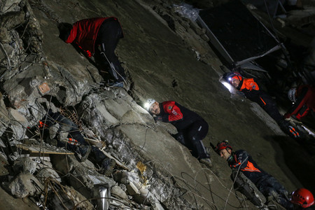 ６日、トルコ南部ハタイ県で、地震により倒壊した建物の壁に耳を当て捜索を続ける救助隊（ＥＰＡ時事）