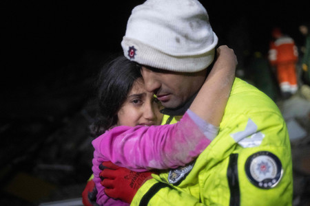 ６日、トルコ南部ハタイ県で、がれきから救助された自分の娘を抱く警官（ＡＦＰ時事）