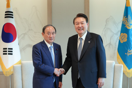 ３１日、ソウルの韓国大統領府で、菅義偉前首相（左）と握手する尹錫悦大統領（大統領府提供）