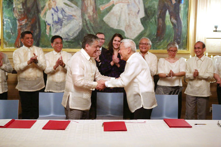 ２３日、ノルウェーの首都オスロで、和平交渉再開で合意し、握手するフィリピン政府代表（手前左）と比共産党関係者（同国政府提供・時事）
