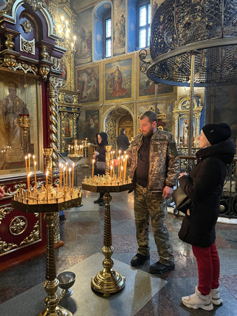 ２４日、ウクライナの首都キーウ（キエフ）旧市街にある聖ミハイル黄金ドーム修道院で、祈りをささげるウクライナ軍兵士ペトロ・バブチュクさん（中央）と妻ウリャナさん