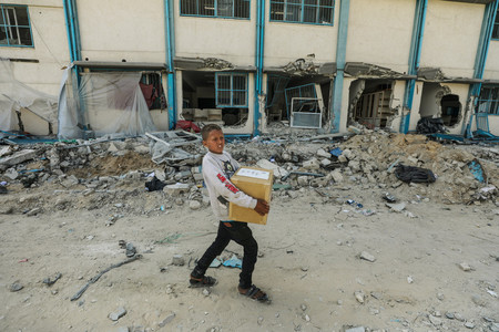 ６日、パレスチナ自治区ガザ南部ハンユニスで、破壊された建物の前を歩く市民（ＥＰＡ時事）