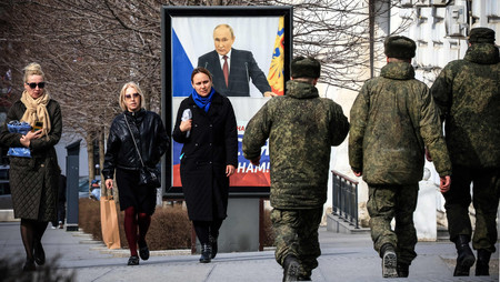 ロシアが一方的に併合したウクライナ南部クリミア半島で、プーチン大統領のポスター前を歩く人々＝２月２９日、シンフェロポリ（ＡＦＰ時事）