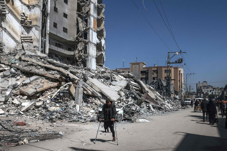 １２日、パレスチナ自治区ガザ南部ラファで、イスラエル軍の空爆で破壊された建物付近を歩く住民（ＡＦＰ時事）