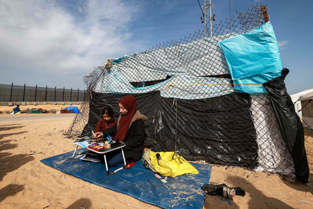 パレスチナ自治区ガザの難民キャンプに設置されたテントの外で絵を描く姉妹＝１７日、南部ラファ（ＡＦＰ時事）