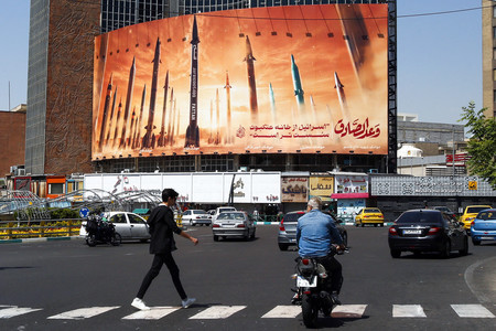 １９日、イランの首都テヘランで、弾道ミサイルが描かれた看板の前を通る市民（ＡＦＰ時事）