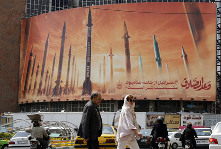イランの首都テヘランで、ミサイルの看板の前を通る市民＝２２日（ＥＰＡ時事）