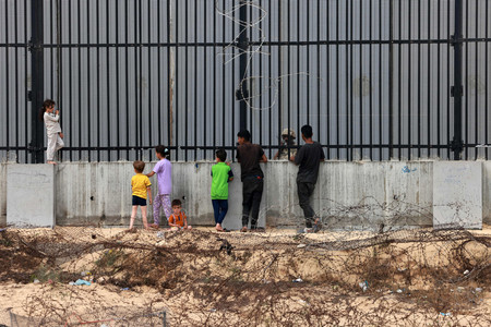 ２６日、パレスチナ自治区ガザ南部ラファで、エジプトとの境界のフェンス越しに会話する子供たちとエジプト兵（ＡＦＰ時事）
