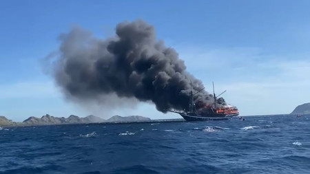 ２日、インドネシアのフローレス島近くの海上で黒煙を上げる観光船（地元警察提供・時事）