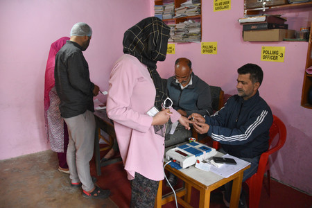 １３日、インド北部カシミール地方スリナガルの投票所で、投票した印のインクを指に塗られる有権者（手前）