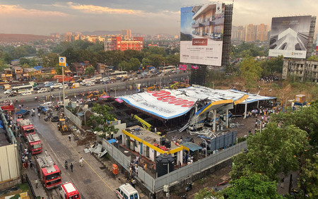 １３日、インド西部ムンバイで、嵐で倒れガソリンスタンドを下敷きにした巨大看板（ロイター時事）