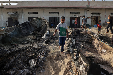 イスラエル軍の空爆を受けて黒焦げになった漁船の間を歩く少年＝２２日、パレスチナ自治区ガザ最南部ラファ（ＡＦＰ時事）