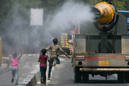 ２８日、熱波に見舞われたインドの首都ニューデリーで、水をまくトラックの後ろを走る子供たち（ＡＦＰ時事）