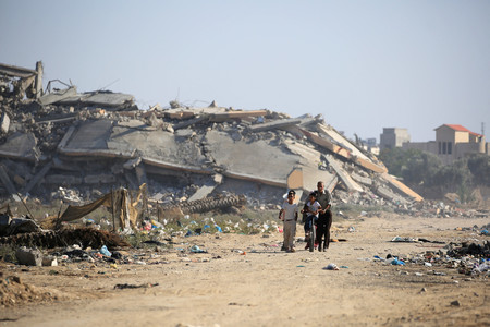 ２日、パレスチナ自治区ガザ中部ブレイジで、破壊された建物のそばを歩く人々（ＡＦＰ時事）