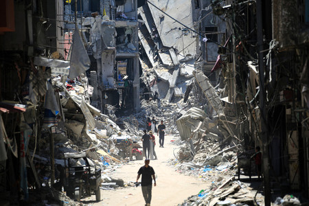 １１日、パレスチナ自治区ガザ南部ハンユニスで破壊された建物の間を歩く住民（ＡＦＰ時事）