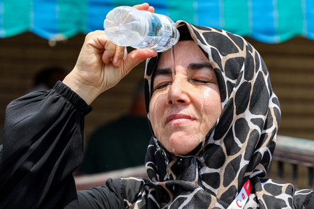 顔に水を掛けて暑さをしのぐ女性＝２０日、サウジアラビア西部メッカ（ＡＦＰ時事）