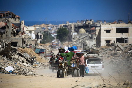 ３日、パレスチナ自治区ガザ南部のハンユニスで、イスラエル軍の攻撃で破壊された建物を通り過ぎる人（ＡＦＰ時事）