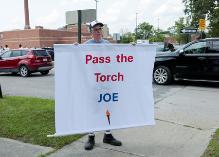 １２日、米中西部ミシガン州デトロイトのバイデン大統領演説会場前で「トーチを渡して」と書いた垂れ幕を掲げるトム・モランさん（ロイター時事）