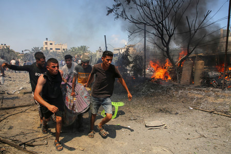 １３日、パレスチナ自治区ガザ南部ハンユニスで、イスラエル軍の攻撃後、犠牲者を運ぶ人々（ロイター時事）