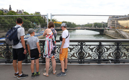 開会式が行われるセーヌ川に架かる橋で、金網越しに川を眺める人々＝２５日、パリ