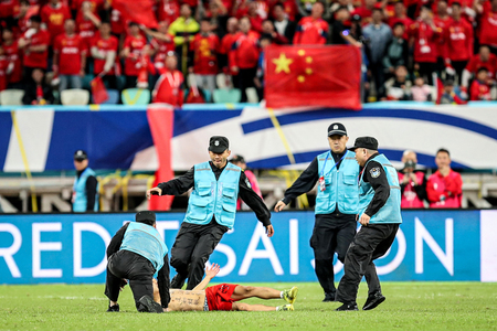 サッカーの日本対中国戦で、ピッチに乱入した男を取り押さえようとする警備員＝１９日、中国福建省アモイ（ＡＦＰ時事）