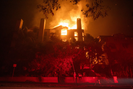 ９日、米西部カリフォルニア州ロサンゼルス近郊の山火事で、炎が上がる家屋（ＡＦＰ時事）