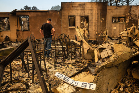 ９日、米西部カリフォルニア州アルタデナで、山火事に巻き込まれた店舗の焼け跡に立つ男性（ＡＦＰ時事）