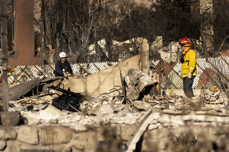 １３日、米カリフォルニア州ロサンゼルスで、山火事で焼けた住宅跡地を捜索する消防隊員ら（ＡＦＰ時事）