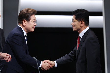 23日、ソウルでのテレビ討論会に先立ち、握手する韓国最大野党「共に民主党」の李在明前代表(左)と金文洙前雇用労働相(EPA時事)