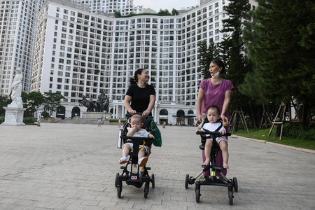 ベビーカーに赤ちゃんを乗せ、マンションの前を歩くベトナムの女性＝２０２２年８月、ハノイ（ＡＦＰ時事）