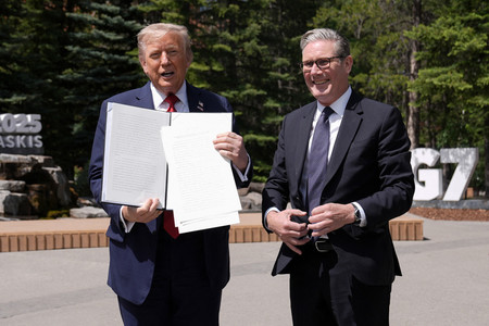 16日、カナダ西部カナナスキスで、貿易協定関連文書を記者団に見せるトランプ米大統領(左)とスターマー英首相(AFP時事)