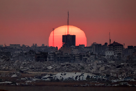 破壊された建物の背後に沈む夕日=1日、イスラエルとパレスチナ自治区ガザの国境からパレスチナ側を撮影(AFP時事)