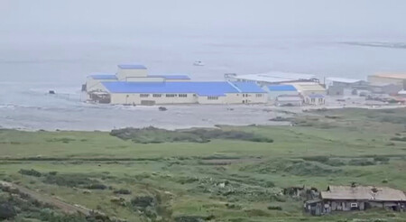 30日、千島列島のパラムシル島セベロクリリスクの海岸沿いの建物に押し寄せる津波(SNSの映像より)(ロイター時事)
