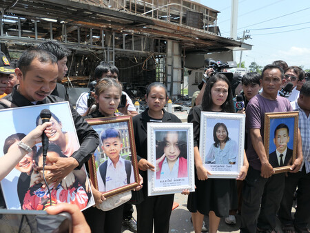 カンボジア軍の砲弾で炎上したタイのコンビニの前で、死亡した家族の写真を持つ遺族ら＝１日、東北部シーサケート県